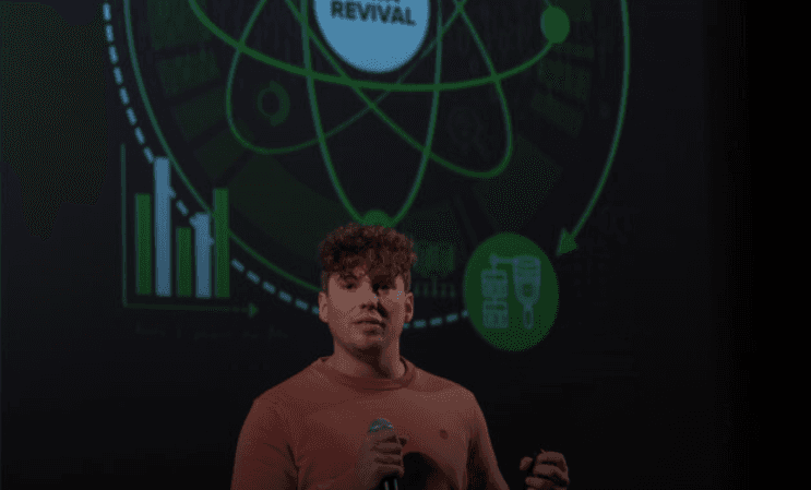 Speaker holding a microphone on stage in front of a projected Data Revival graphic